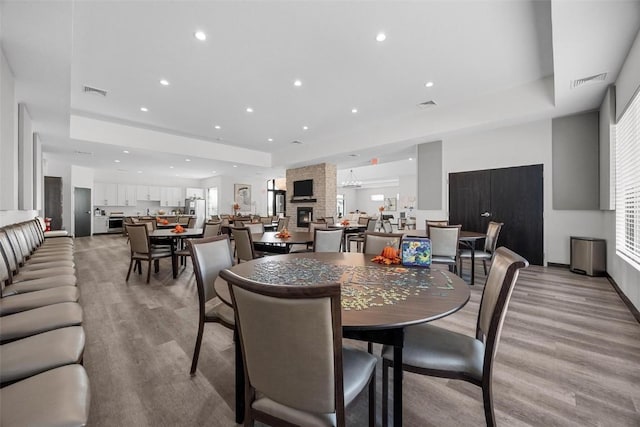 dining room with a raised ceiling, a fireplace, and light wood-type flooring