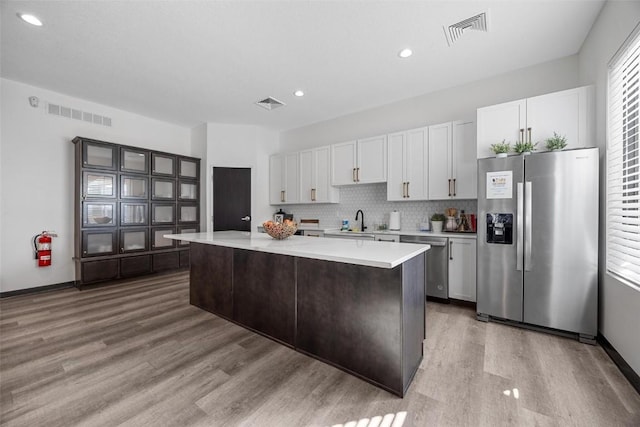 kitchen with appliances with stainless steel finishes, a center island, wood-type flooring, white cabinets, and decorative backsplash