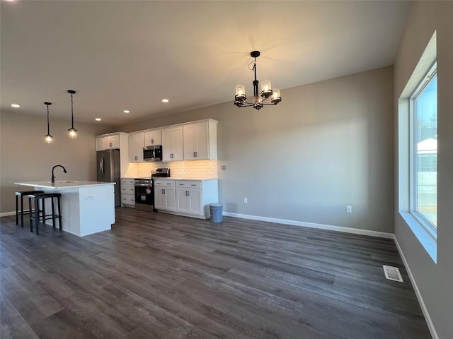 kitchen featuring a breakfast bar, white cabinetry, pendant lighting, stainless steel appliances, and a kitchen island with sink