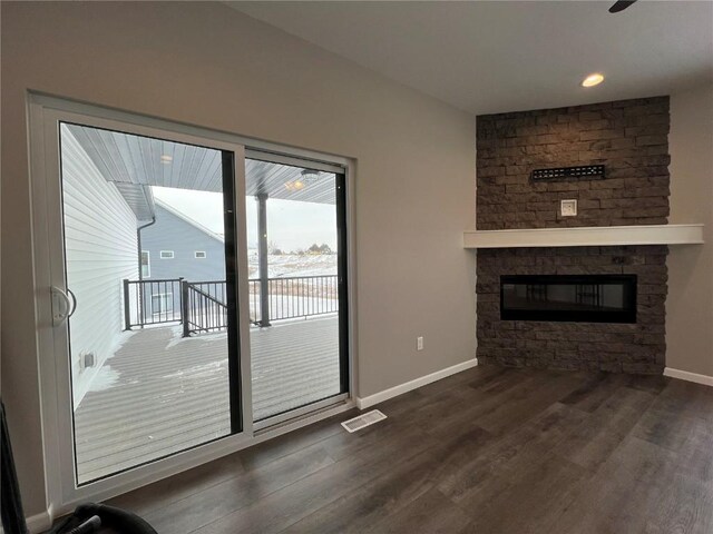 unfurnished living room featuring a stone fireplace and dark hardwood / wood-style floors