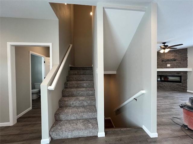 staircase featuring wood-type flooring, a large fireplace, and ceiling fan