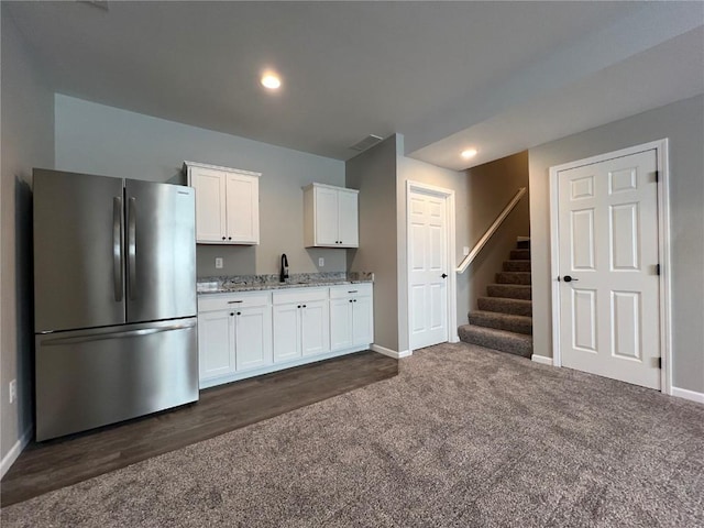 kitchen with sink, stainless steel refrigerator, dark colored carpet, light stone countertops, and white cabinets