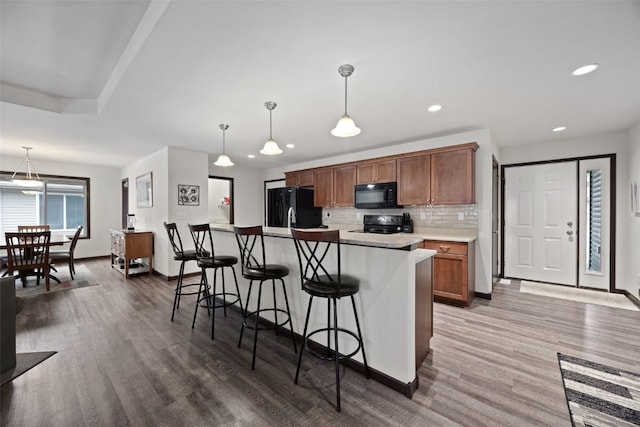 kitchen featuring a kitchen island, decorative light fixtures, a kitchen breakfast bar, decorative backsplash, and black appliances