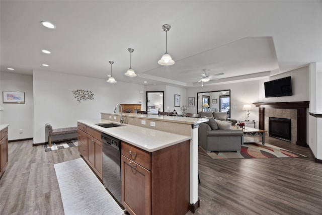 kitchen with pendant lighting, sink, dishwasher, wood-type flooring, and an island with sink