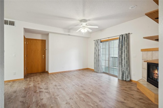 unfurnished living room with a tiled fireplace, hardwood / wood-style floors, a textured ceiling, and ceiling fan