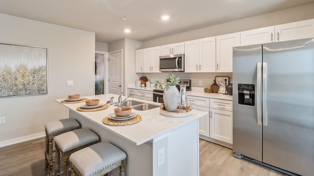 kitchen featuring sink, a kitchen island with sink, white cabinetry, stainless steel appliances, and light wood-type flooring