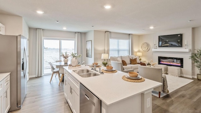 kitchen with appliances with stainless steel finishes, sink, white cabinets, hardwood / wood-style flooring, and a center island with sink