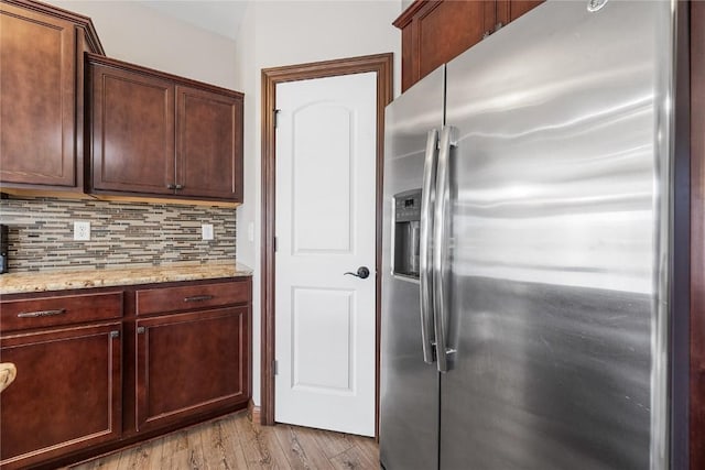 kitchen with light stone countertops, decorative backsplash, light wood-type flooring, and stainless steel fridge with ice dispenser