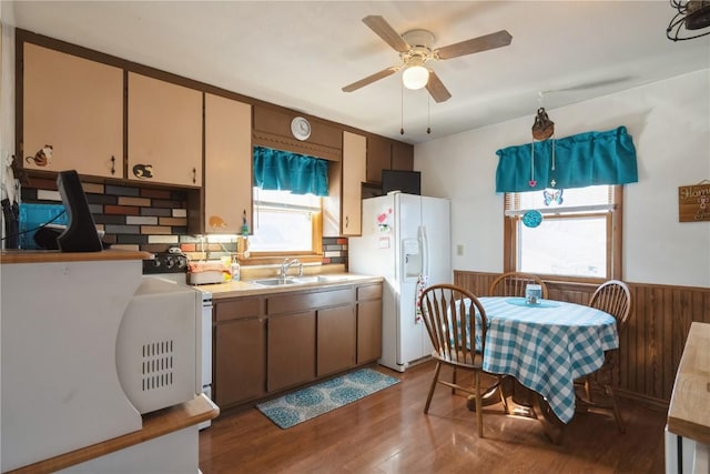 kitchen with sink, wood walls, dark hardwood / wood-style flooring, white fridge with ice dispenser, and ceiling fan