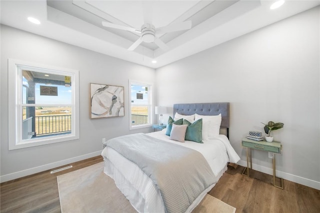 bedroom featuring hardwood / wood-style flooring, ceiling fan, a tray ceiling, and multiple windows