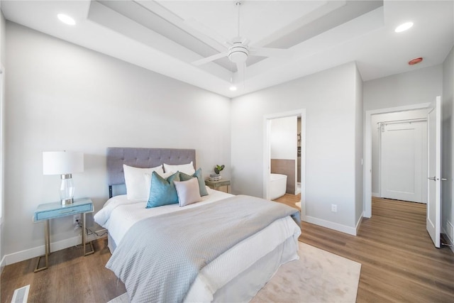 bedroom with a raised ceiling, ensuite bathroom, and hardwood / wood-style floors