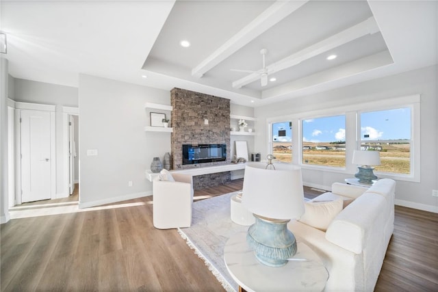 living room with ceiling fan, a stone fireplace, a raised ceiling, and hardwood / wood-style floors