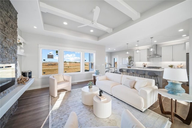 living room with ceiling fan, a stone fireplace, beam ceiling, and light hardwood / wood-style flooring