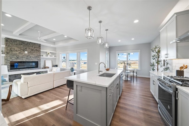 kitchen with sink, an island with sink, pendant lighting, stainless steel appliances, and light stone countertops