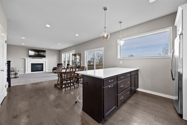 kitchen with stainless steel refrigerator, dark hardwood / wood-style flooring, a kitchen breakfast bar, hanging light fixtures, and dark brown cabinetry