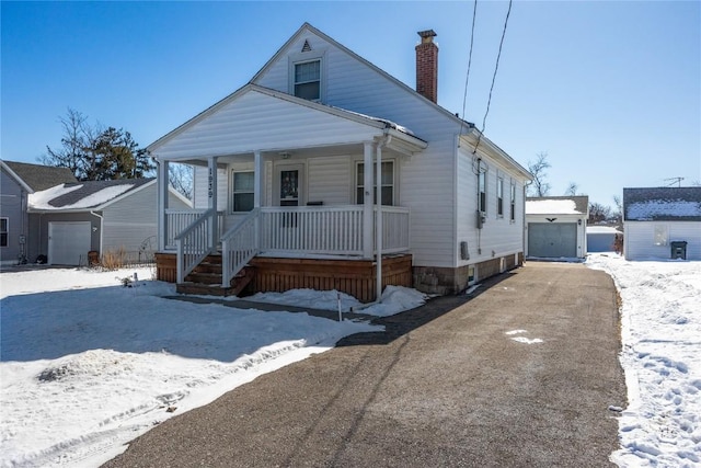 view of front of home with covered porch, aphalt driveway, a chimney, and a garage