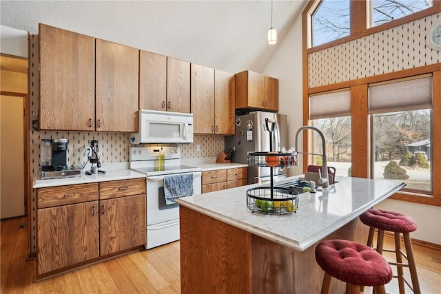 kitchen featuring a breakfast bar, an island with sink, sink, hanging light fixtures, and white appliances