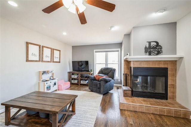 living room featuring a tiled fireplace, hardwood / wood-style floors, and ceiling fan