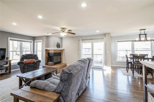 living room with hardwood / wood-style flooring, a tiled fireplace, ceiling fan with notable chandelier, and a wealth of natural light