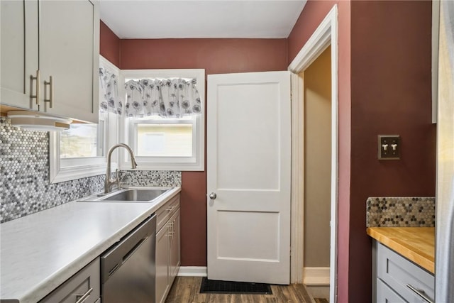 kitchen featuring tasteful backsplash, stainless steel dishwasher, dark wood-type flooring, a sink, and baseboards