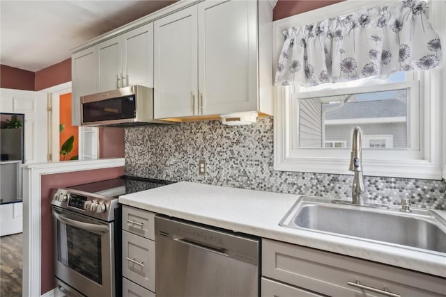 kitchen featuring appliances with stainless steel finishes, light countertops, a sink, and tasteful backsplash