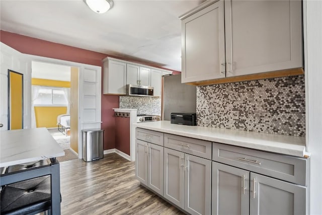 kitchen with light countertops, light wood-type flooring, gray cabinets, decorative backsplash, and stainless steel microwave