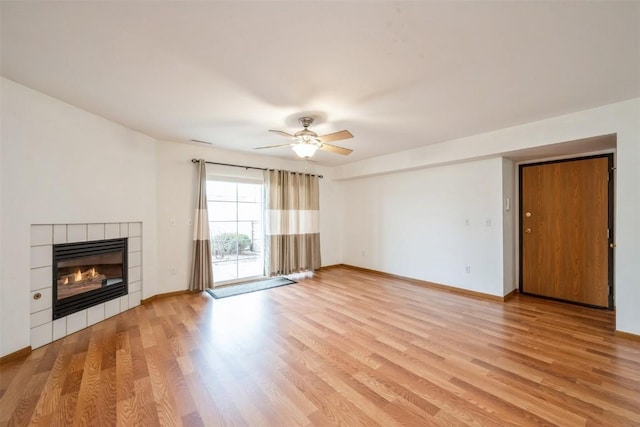 unfurnished living room with a tile fireplace, ceiling fan, and light wood-type flooring