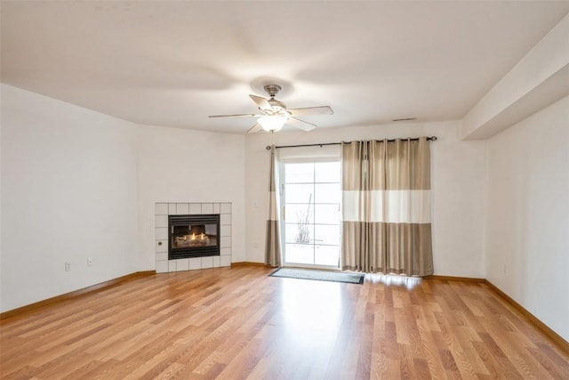 unfurnished living room with a tile fireplace, ceiling fan, and light wood-type flooring