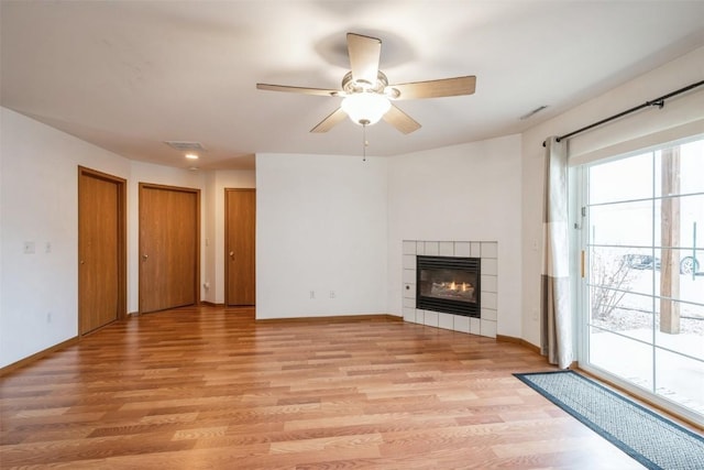 unfurnished living room featuring a tile fireplace, ceiling fan, and light wood-type flooring