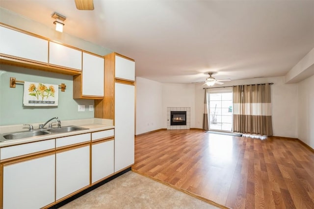 kitchen featuring sink, ceiling fan, a fireplace, light hardwood / wood-style floors, and white cabinets