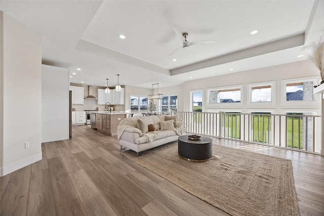 living room featuring ceiling fan, sink, light hardwood / wood-style floors, and a tray ceiling