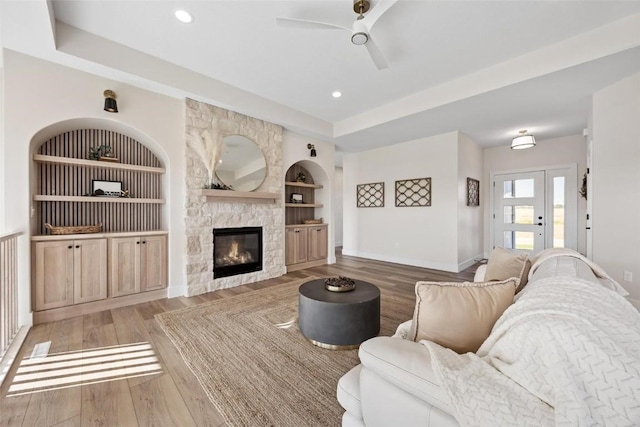 living room featuring hardwood / wood-style flooring, a stone fireplace, a raised ceiling, and built in features