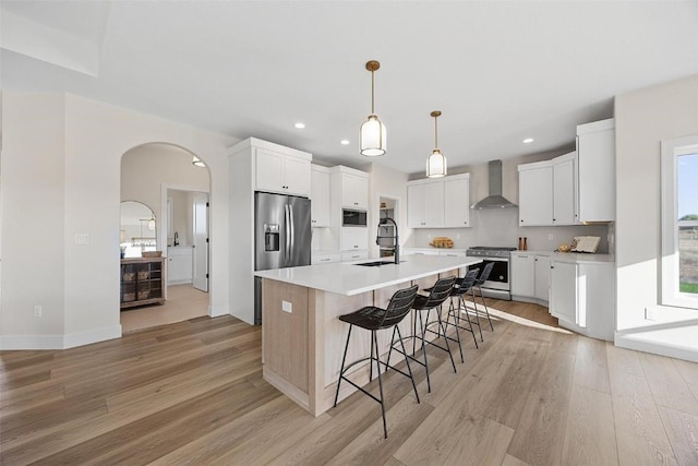 kitchen featuring sink, stainless steel appliances, white cabinets, a center island with sink, and wall chimney exhaust hood