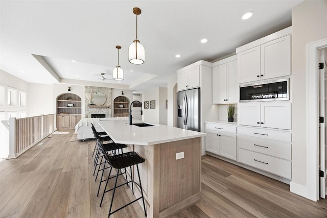 kitchen with sink, white cabinetry, stainless steel fridge, pendant lighting, and a kitchen island with sink