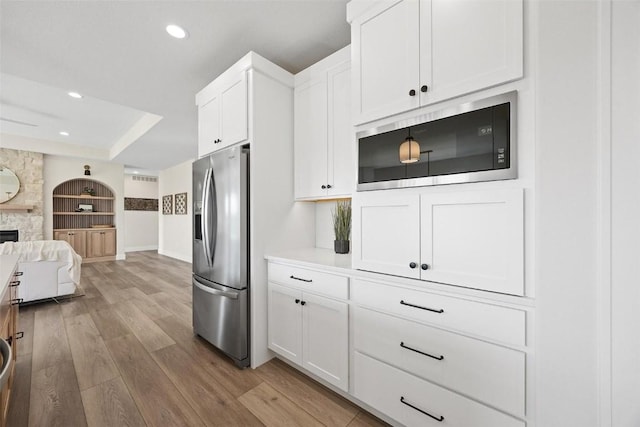 kitchen with stainless steel refrigerator with ice dispenser, white cabinetry, light wood-type flooring, and built in microwave