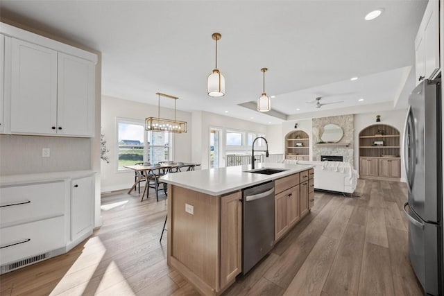 kitchen featuring appliances with stainless steel finishes, white cabinetry, an island with sink, sink, and hanging light fixtures