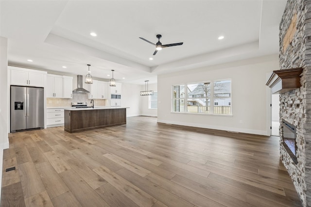 kitchen featuring stainless steel appliances, a tray ceiling, a kitchen island with sink, and wall chimney exhaust hood