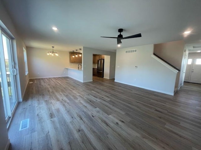 unfurnished living room featuring wood-type flooring and ceiling fan with notable chandelier