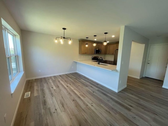 kitchen featuring pendant lighting, appliances with stainless steel finishes, wood-type flooring, decorative backsplash, and kitchen peninsula