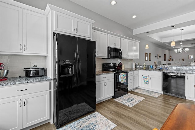 kitchen featuring hanging light fixtures, black appliances, white cabinets, and light stone countertops