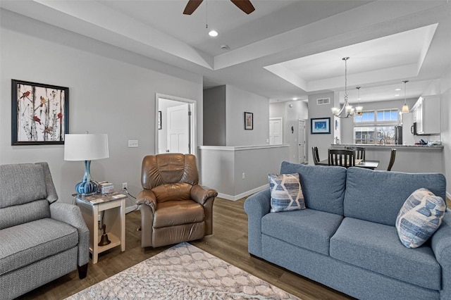 living room featuring ceiling fan with notable chandelier, dark wood-type flooring, and a raised ceiling