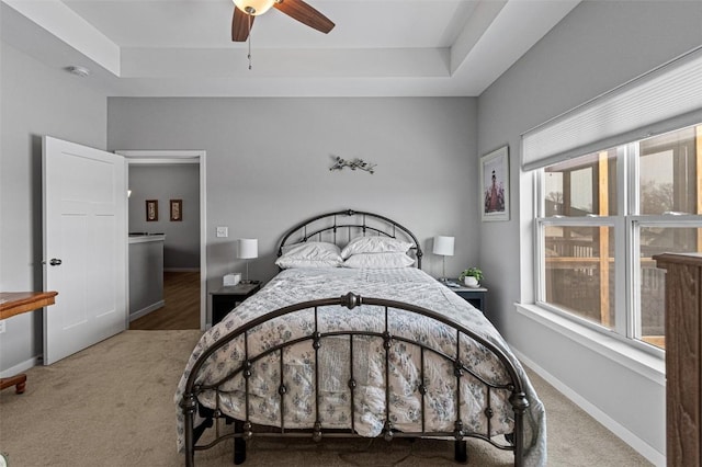 carpeted bedroom with ceiling fan and a tray ceiling