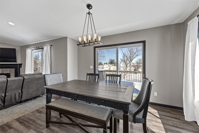 dining space featuring a tiled fireplace, hardwood / wood-style floors, and an inviting chandelier