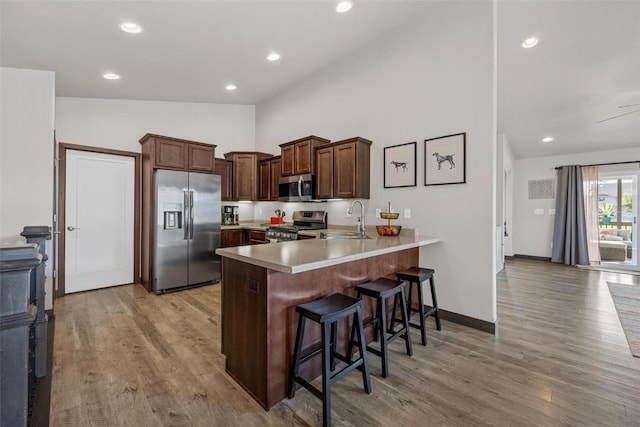 kitchen with a kitchen bar, sink, light wood-type flooring, appliances with stainless steel finishes, and kitchen peninsula