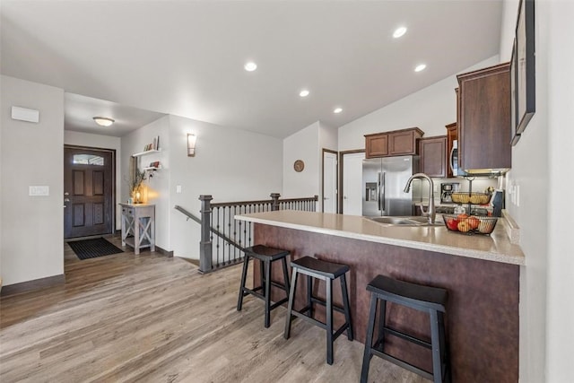 kitchen featuring sink, stainless steel fridge, a breakfast bar area, kitchen peninsula, and light wood-type flooring