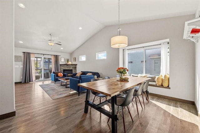 dining room with dark hardwood / wood-style floors, ceiling fan, a stone fireplace, and high vaulted ceiling