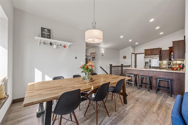 dining room featuring lofted ceiling, sink, and light wood-type flooring