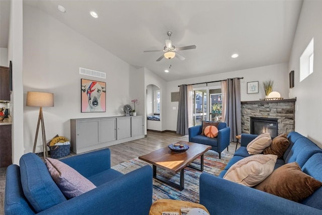 living room featuring ceiling fan, a stone fireplace, high vaulted ceiling, and light hardwood / wood-style flooring