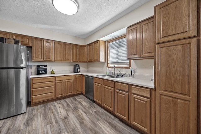 kitchen featuring appliances with stainless steel finishes, sink, a textured ceiling, and light wood-type flooring