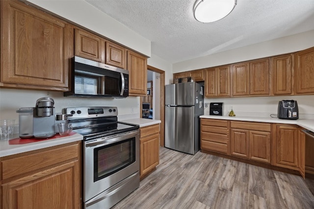 kitchen featuring stainless steel appliances, a textured ceiling, and light wood-type flooring